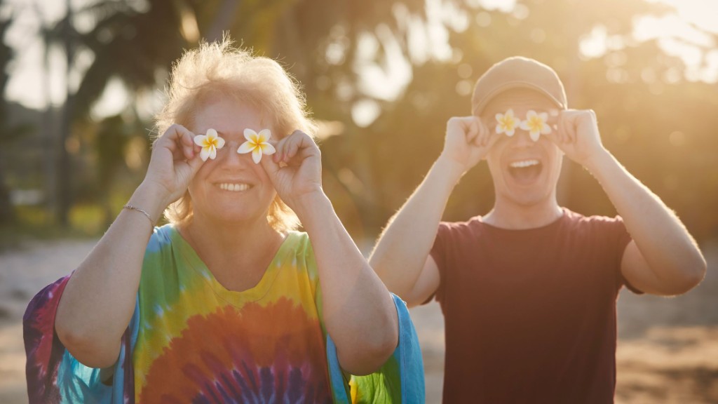 Two people smiling outdoors, playfully holding plumeria flowers over their eyes