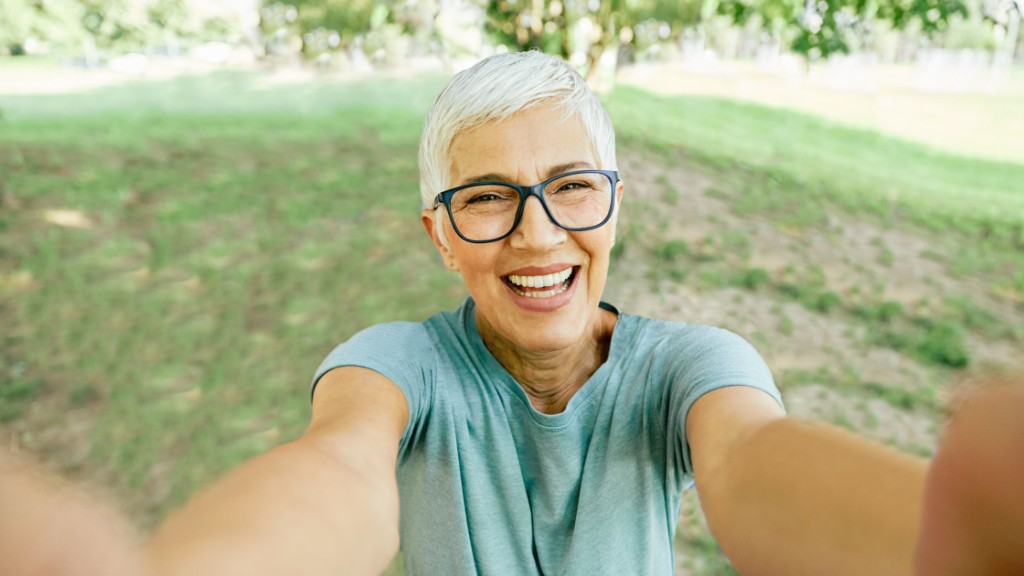 Smiling older adult in eyeglasses outdoors, taking a sunny selfie