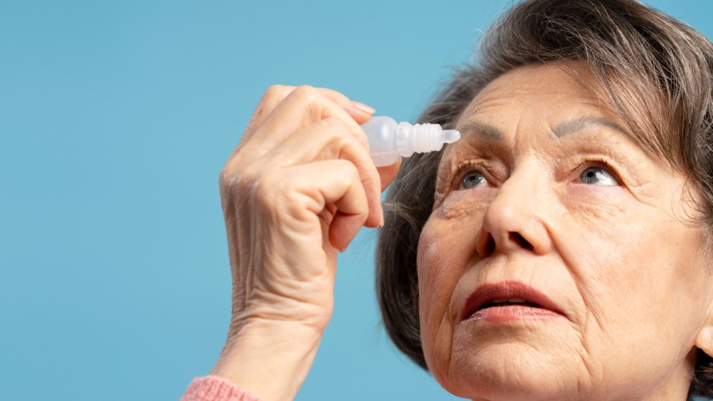Older adult applying eye drops from a small bottle against a calm blue background